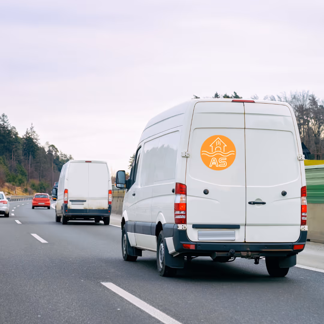 Weiße Lieferwagen fahren auf einer Autobahn mit Bäumen und Gebäuden im Hintergrund.